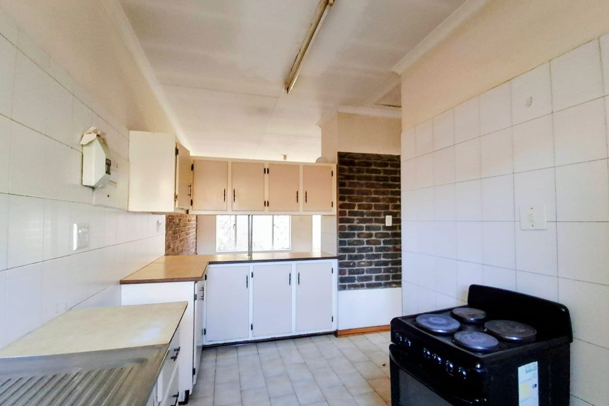 A dated kitchen featuring built-in cabinetry, tiled surfaces, and an exposed brick accent wall, offering a functional layout ready for modernization.