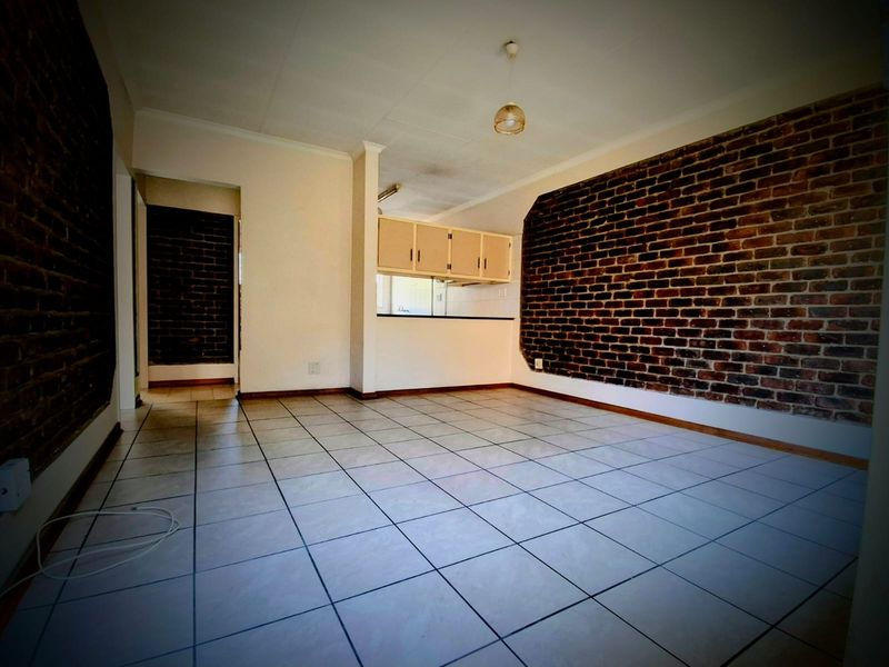 An open-plan living and kitchen area featuring exposed brick feature walls and tiled flooring, presenting a blank canvas for interior design.