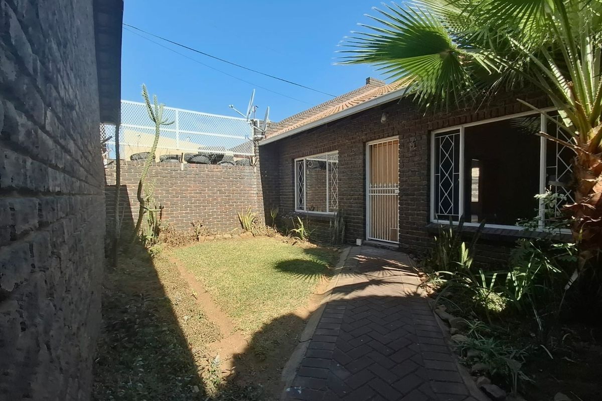 A rear exterior view of the apartment featuring a brick facade, a paved walkway, and a small private garden area with boundary walling.