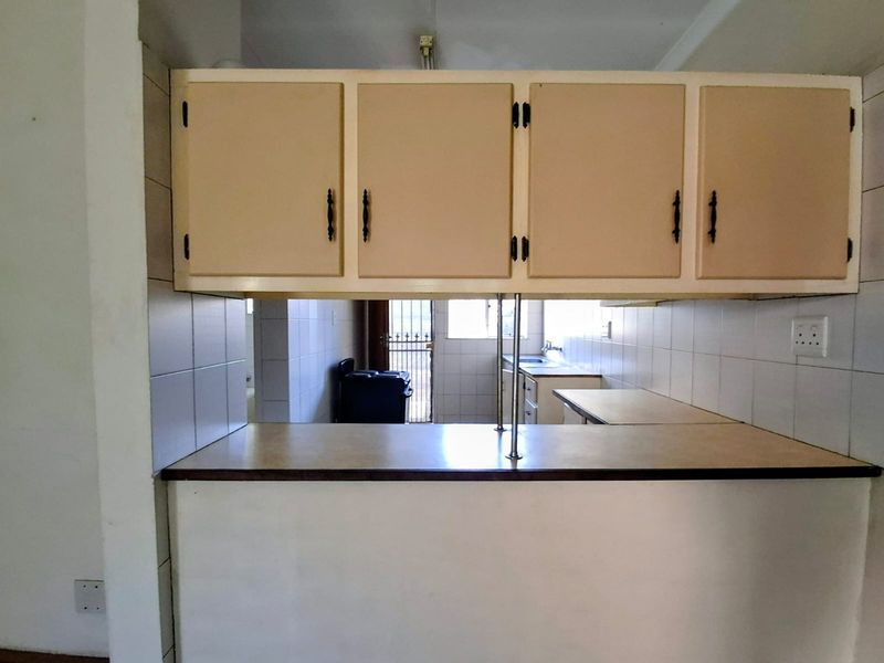 A dated kitchen featuring built-in cabinetry, a tiled splashback, and a breakfast bar counter, offering a functional layout with potential for modernization.