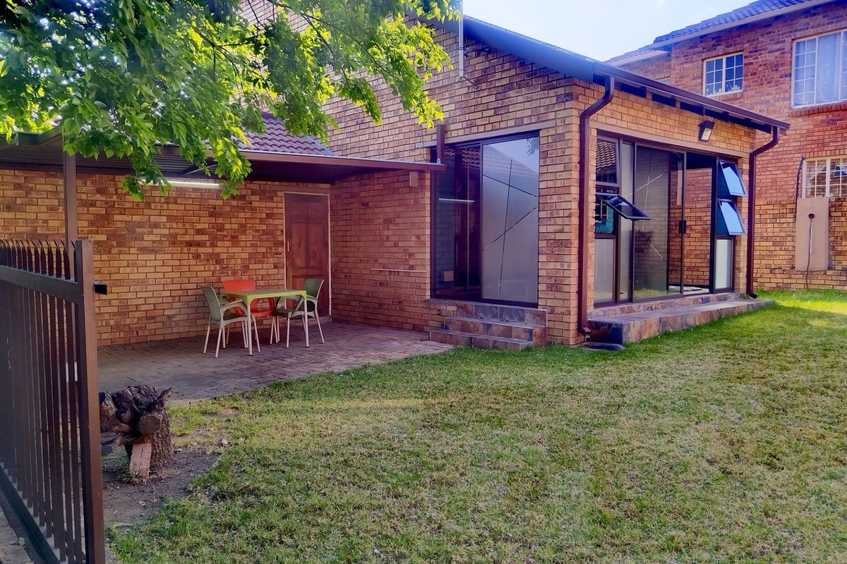 Rear view of a face brick townhouse featuring a covered patio, paved outdoor area, and a private lawn with sliding door access.