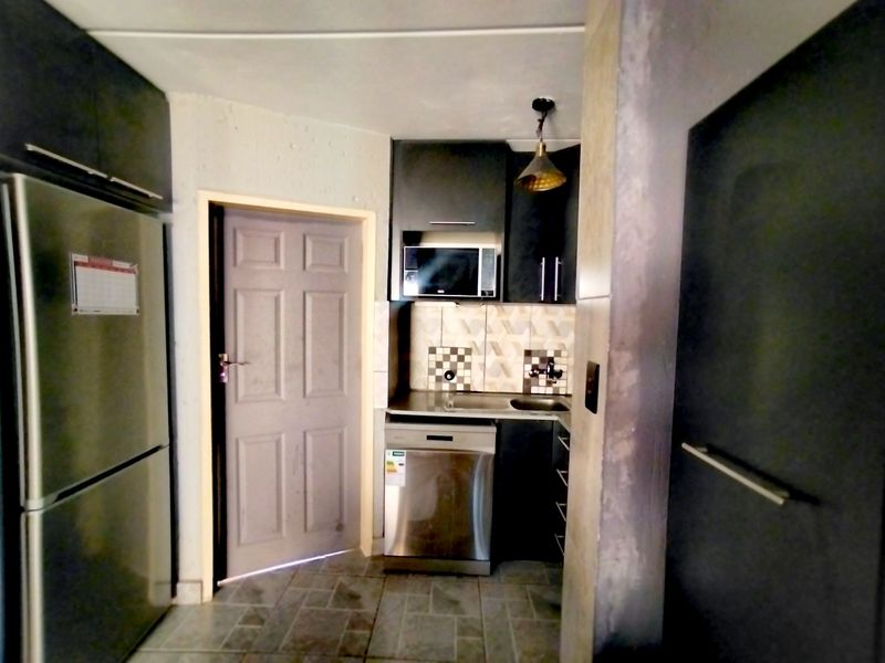Compact scullery area featuring dark built-in cabinetry, stainless steel sink, integrated dishwasher, and built-in microwave with tiled backsplash and flooring.