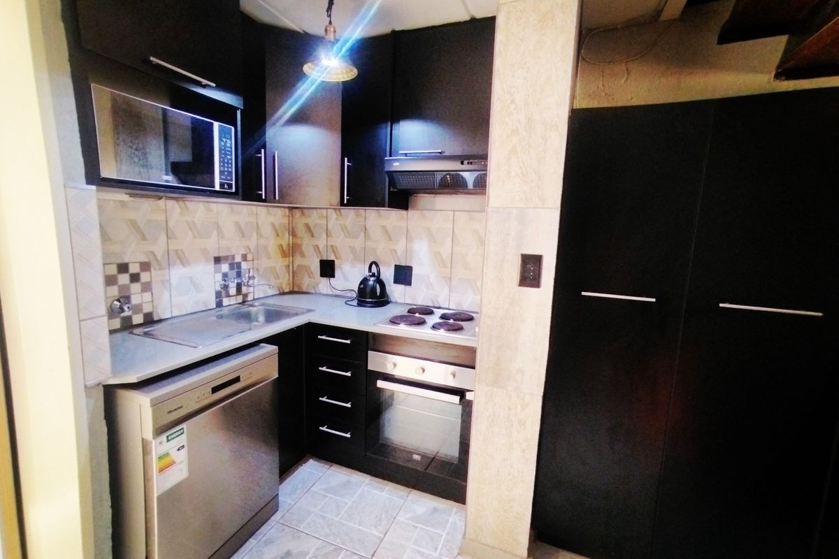 Compact kitchen featuring dark cabinetry, integrated appliances including an oven and hob, tiled backsplash, and durable floor tiling.