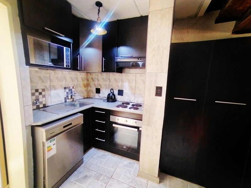 Compact kitchen featuring dark cabinetry, integrated appliances including an oven and hob, tiled backsplash, and durable floor tiling.