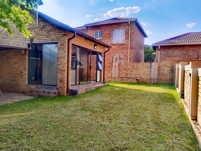 Rear view of a face brick townhouse featuring a private garden, tiled patio area, and large sliding glass doors providing access to the interior.