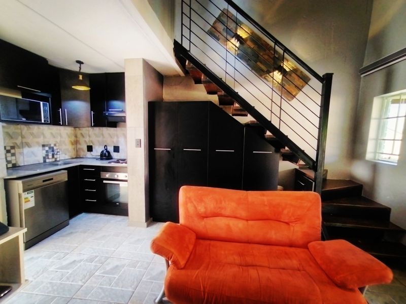 Open-plan kitchen and living area featuring modern dark cabinetry, built-in appliances, and a striking staircase with metal balustrades.