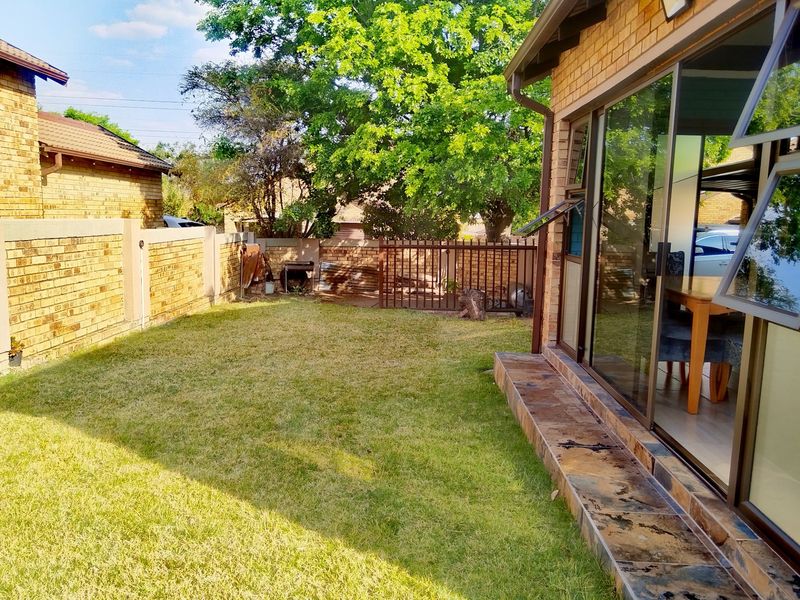 A private rear garden featuring a lawn, brick boundary walls, and a tiled patio area accessible through sliding glass doors.