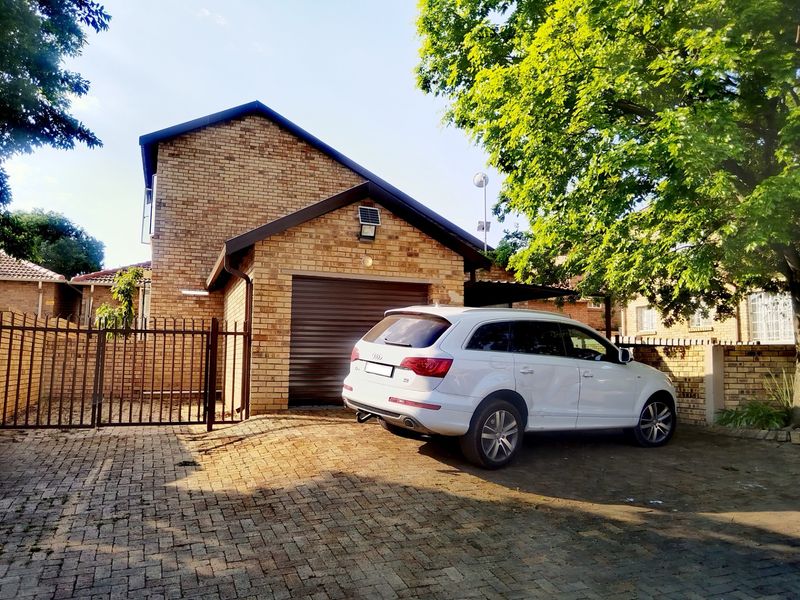 Front exterior view of a brick townhouse featuring a paved driveway, secure metal gate, and a single roller garage door.
