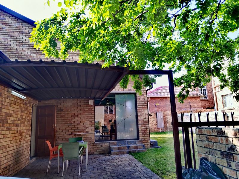 A covered brick patio area featuring paved flooring and a sliding glass door entrance, set within a private garden space.
