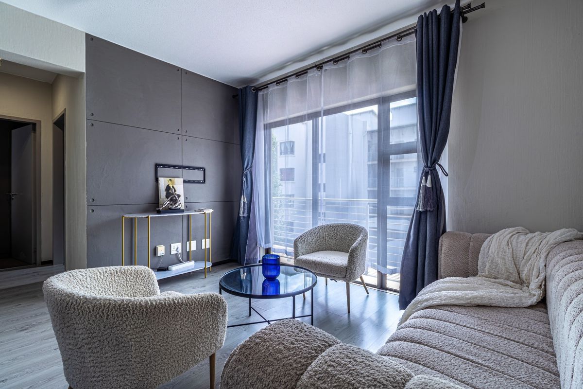 A modern living room featuring a dark grey feature wall, laminate flooring, and a large sliding glass door providing access to the balcony.