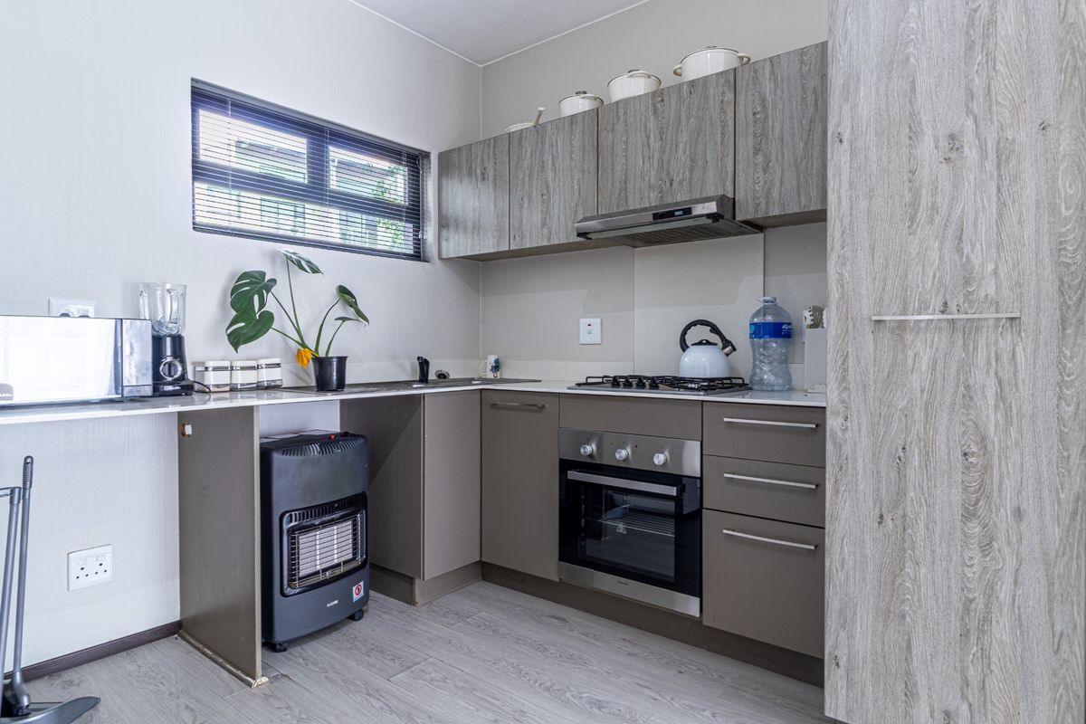Modern kitchen featuring wood-grain cabinetry, built-in gas hob, electric oven, extractor fan, and laminate flooring with a functional layout.