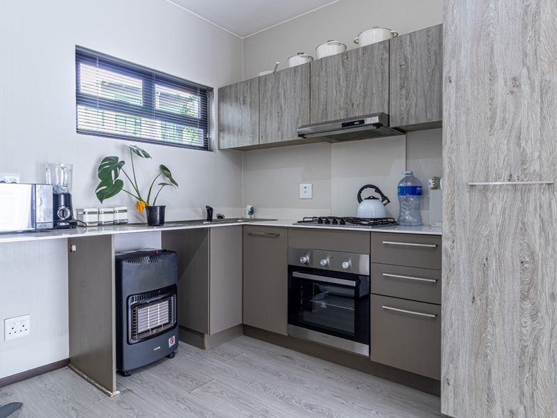 Modern kitchen featuring wood-grain cabinetry, built-in gas hob, electric oven, extractor fan, and laminate flooring with a functional layout.
