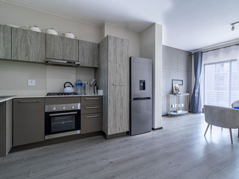 Modern open-plan kitchen and living area featuring contemporary cabinetry, integrated appliances, laminate flooring, and direct access to a balcony.