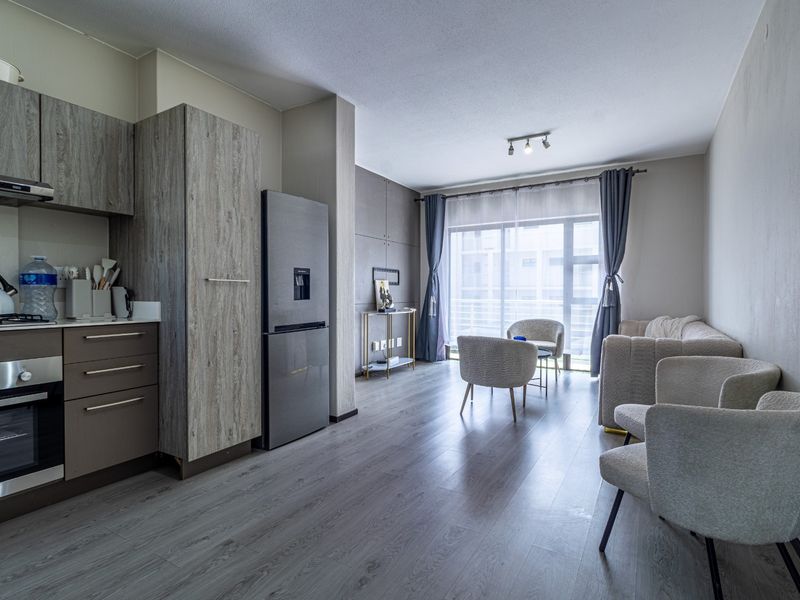 Modern open-plan living area featuring a contemporary kitchen with wood-grain cabinetry, integrated appliances, and seamless flow to a bright lounge with sliding door access.