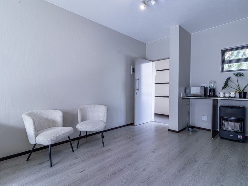 A neutrally painted living area featuring laminate flooring, a window with blinds, and access to an adjacent room.