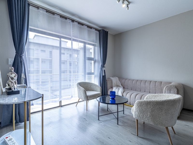 A bright and modern living room featuring laminate flooring and a large sliding glass door that opens to a balcony.