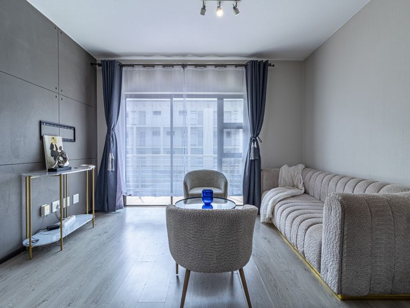 A modern living room featuring laminate flooring, a decorative feature wall, and a large sliding glass door providing access to the balcony.