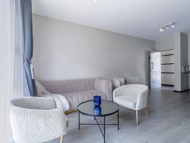 A bright and modern living room featuring light-toned laminate flooring, neutral wall finishes, and integrated track lighting, creating a clean and inviting atmosphere.
