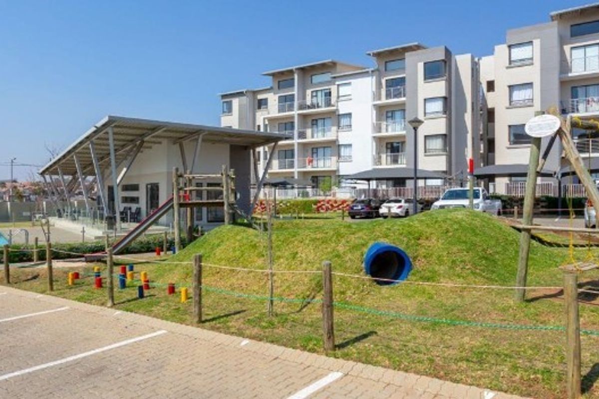 Exterior view of the apartment complex featuring a landscaped playground area, paved parking, and communal recreational facilities.