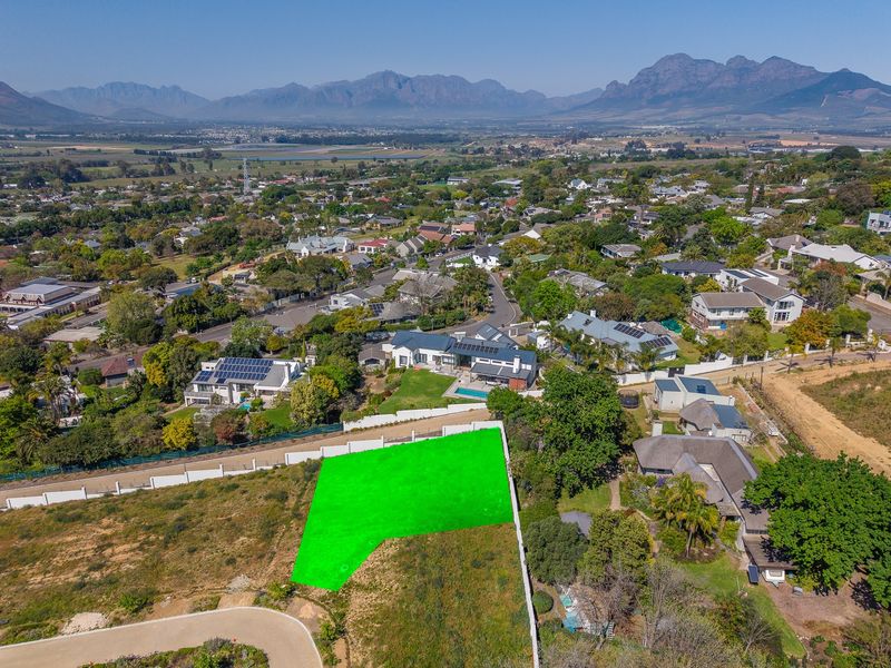 Aerial view of a vacant residential plot highlighted in green, situated in a developed neighborhood with mountain views.