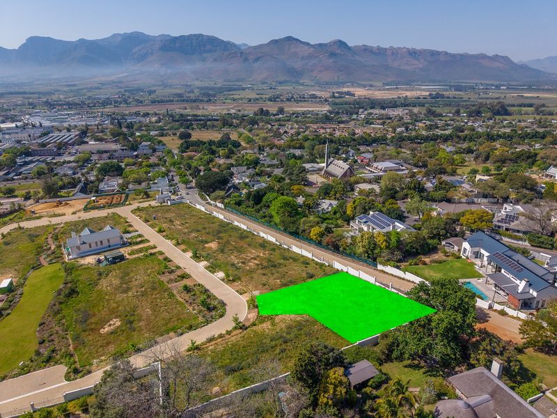 Aerial view of a vacant residential plot highlighted in green, situated in a developed neighborhood with mountain views and established infrastructure.