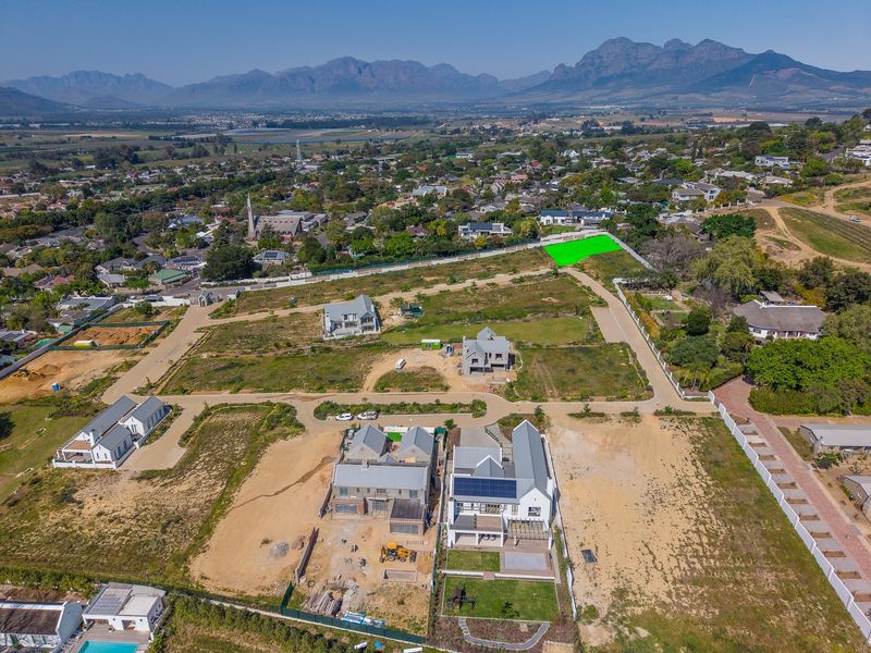 Aerial view of a residential development estate featuring vacant plots, newly constructed homes, and surrounding mountain landscape.