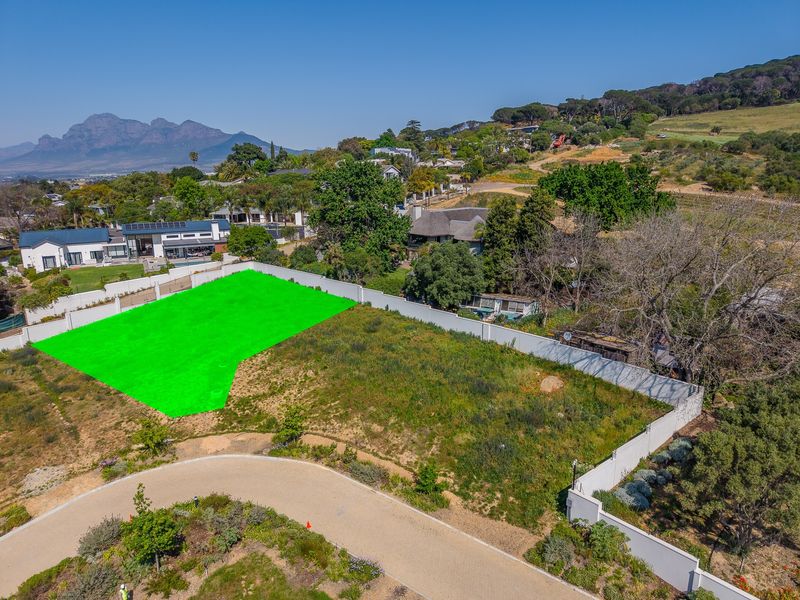 Aerial view of a vacant residential plot featuring a perimeter wall and paved access road in a scenic estate setting.