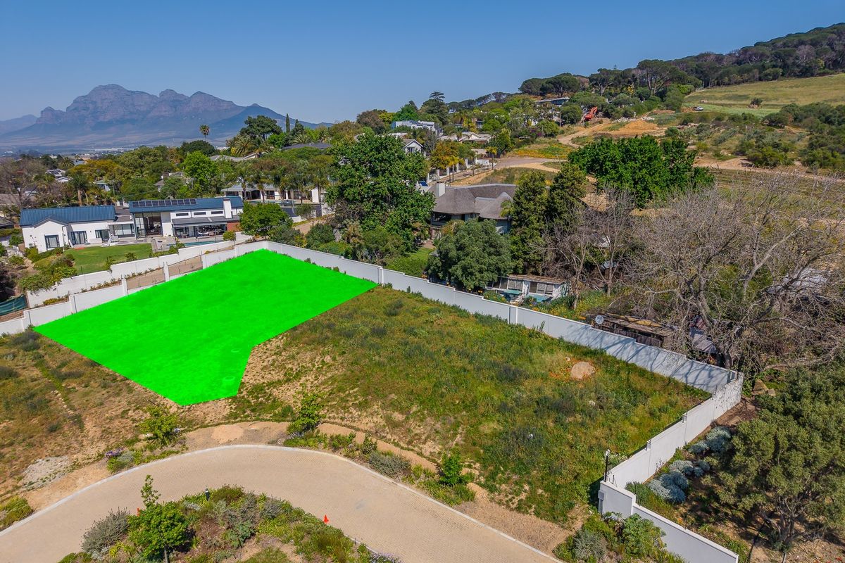 Aerial view of a vacant residential plot featuring a perimeter wall and paved access road in a scenic estate setting.