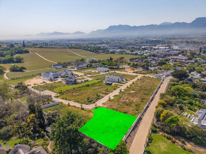Aerial view of a vacant residential plot in a developed estate, featuring clear boundary lines, paved access, and scenic mountain views.