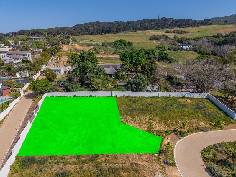 Aerial view of a vacant residential plot featuring a perimeter wall and adjacent paved access road in a scenic landscape setting.