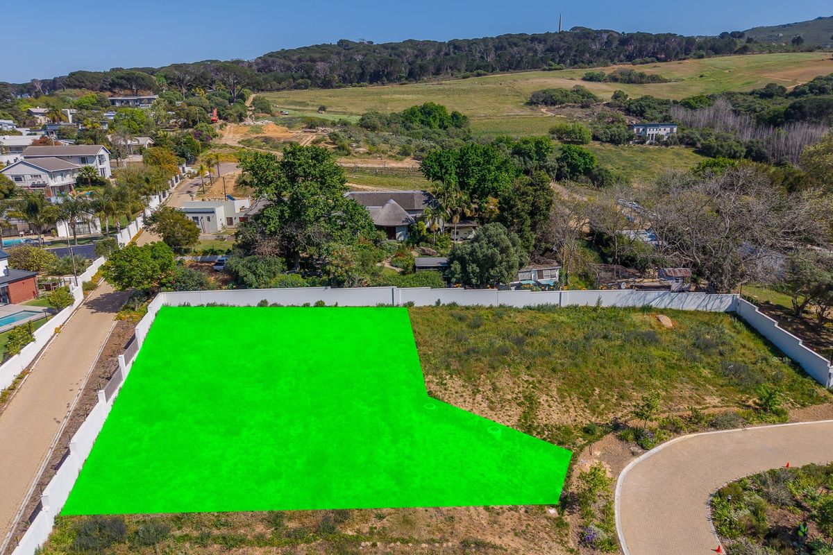 Aerial view of a vacant residential plot featuring a perimeter wall and adjacent paved access road in a scenic landscape setting.