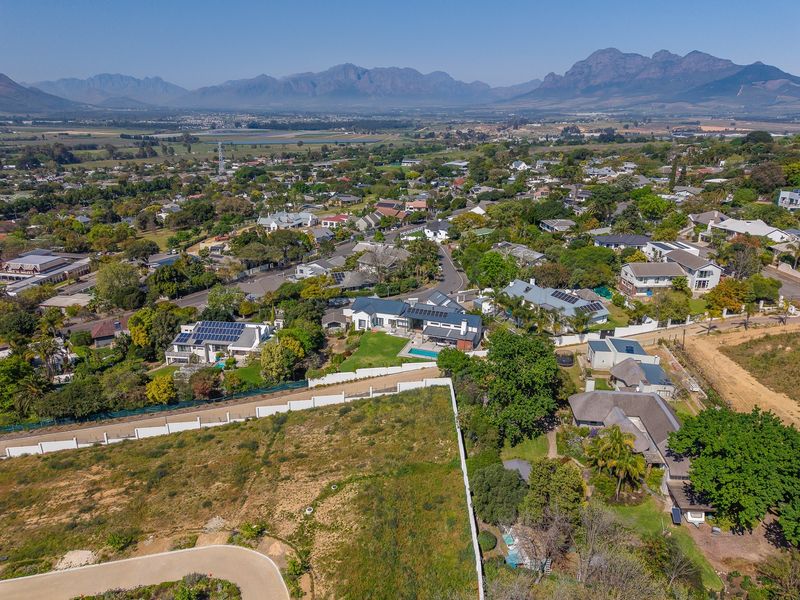 Aerial view of a vacant residential plot featuring boundary walls and a paved driveway, situated in a developed suburban neighborhood with mountain views.