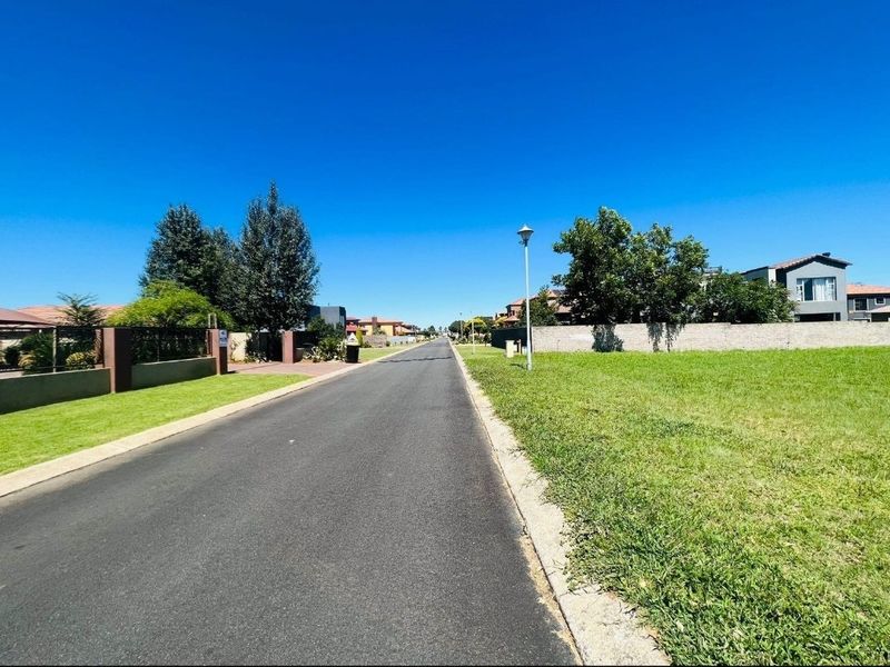 A clear street view of a residential neighborhood featuring paved roads, concrete curbing, and established boundary walls.