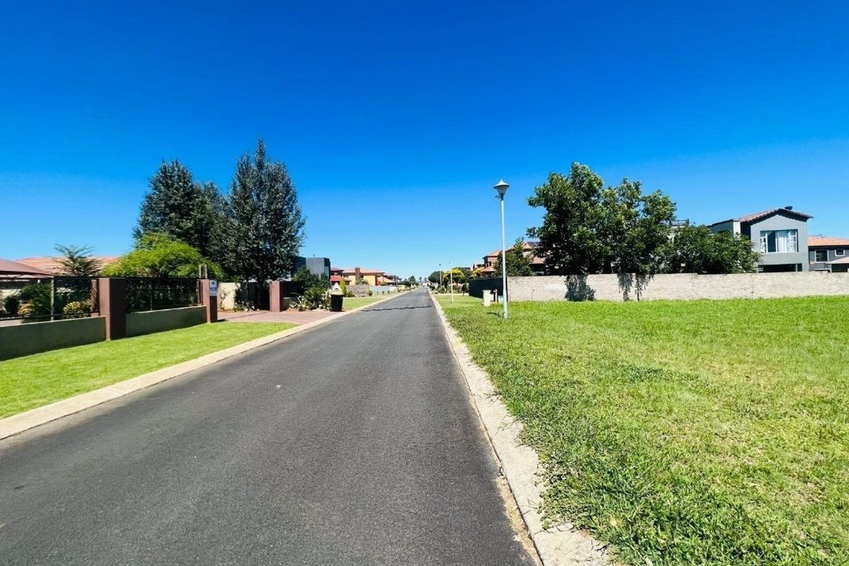 A clear street view of a residential neighborhood featuring paved roads, concrete curbing, and established boundary walls.