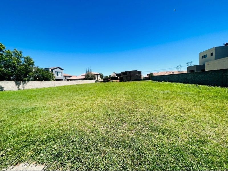 A vacant residential plot featuring a level grass lawn enclosed by perimeter boundary walls in a developed neighborhood.