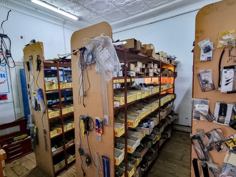 A commercial utility or storage space featuring built-in shelving units, pressed metal ceilings, and fluorescent lighting, currently used for inventory storage.