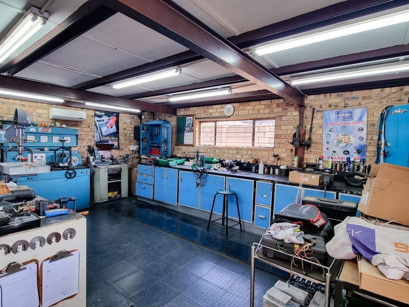 A functional commercial workshop space featuring exposed steel beams, durable rubber flooring, brick walls, and extensive built-in cabinetry and workbench areas.