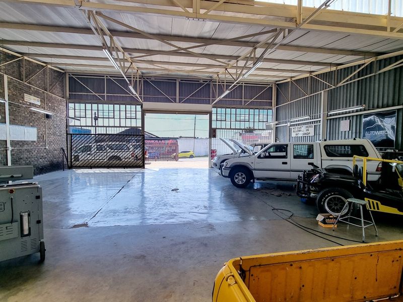 Spacious commercial workshop featuring high ceilings with exposed steel trusses, durable epoxy flooring, and large sliding gate access for vehicle entry.