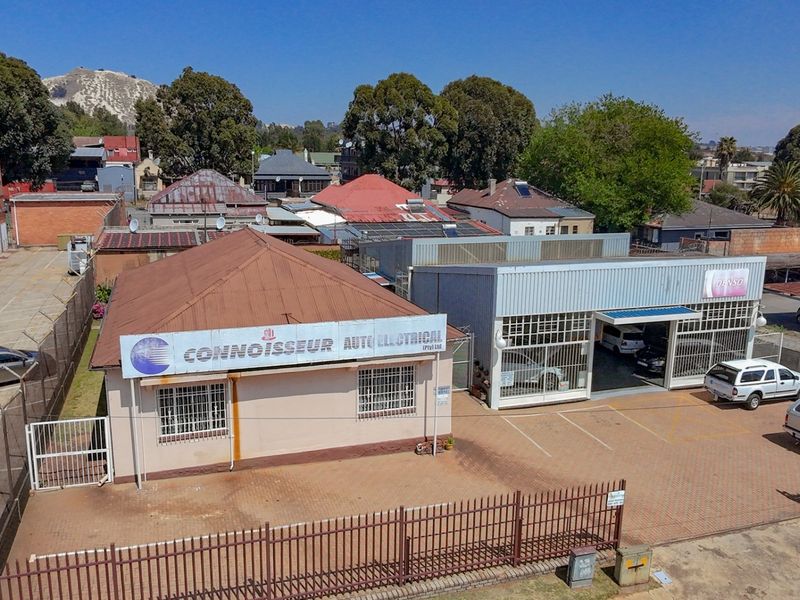Aerial view of a commercial property featuring a workshop building with metal roofing, paved parking area, and secure perimeter fencing.