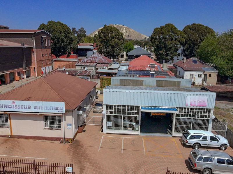 Aerial view of a commercial property featuring multiple workshop buildings, paved parking, and secure perimeter fencing in an urban setting.
