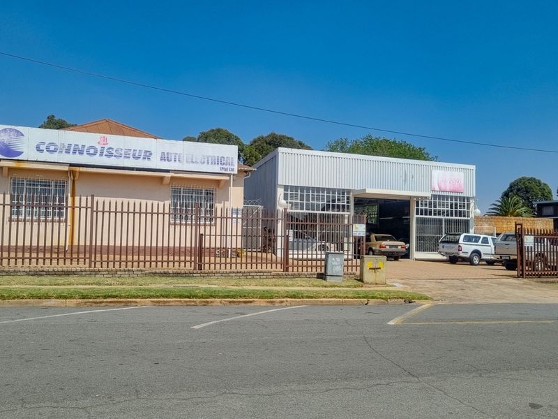 Front view of a commercial auto electrical workshop featuring secure perimeter fencing, paved driveway access, and prominent business signage.