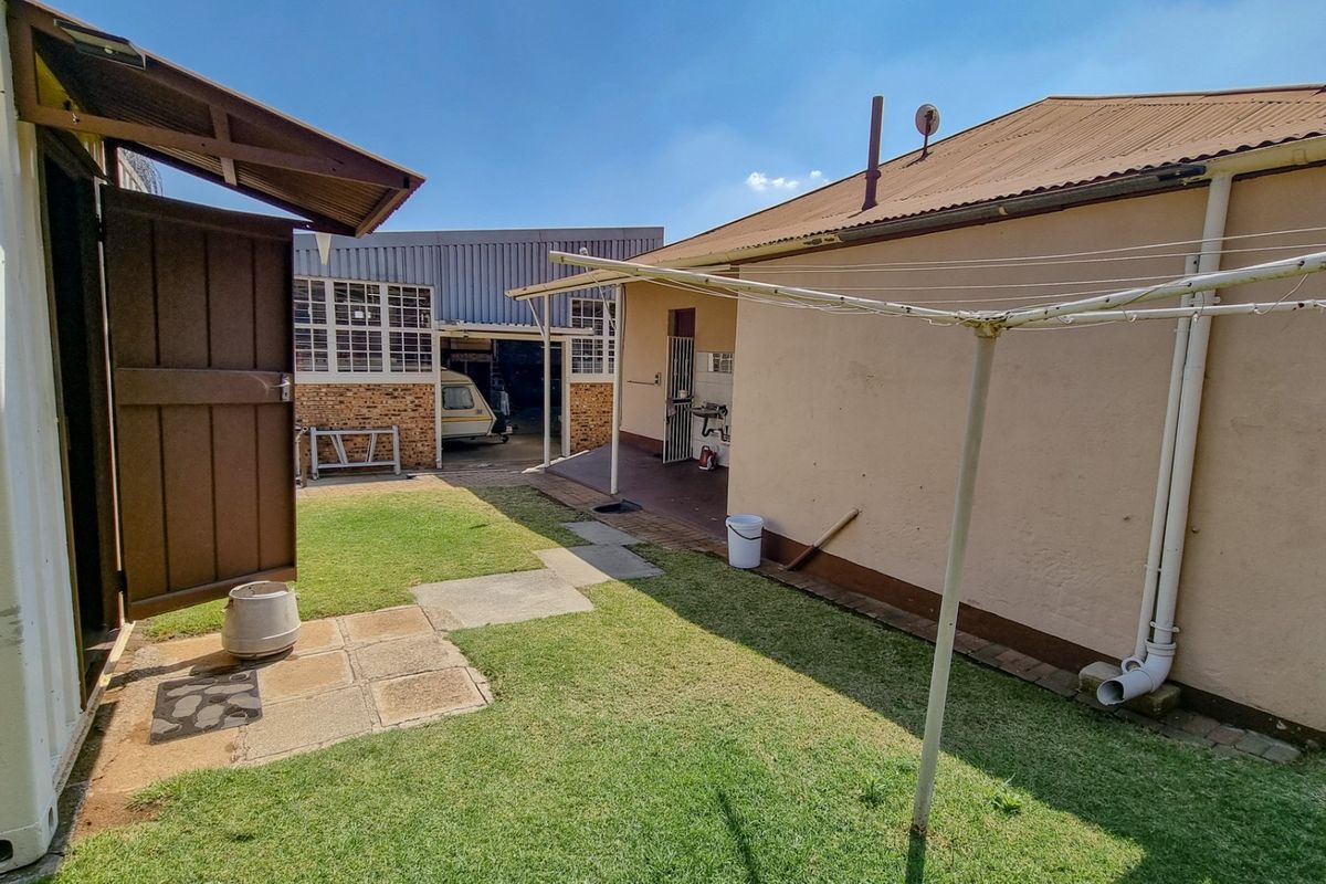 Rear exterior view of the commercial property featuring a lawn, paved walkway, and corrugated metal roofing with access to a rear workshop area.