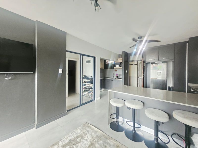 Modern open-plan living area featuring a sleek kitchen with stone countertops, a breakfast bar, and tiled flooring throughout.