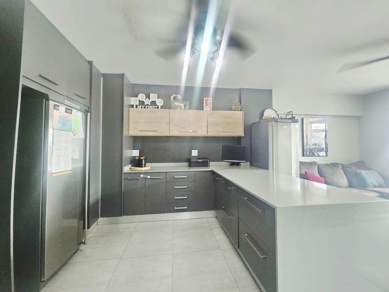 Modern open-plan kitchen featuring sleek dark cabinetry, light wood accents, stone countertops, and tiled flooring, seamlessly integrated with the adjacent living area.