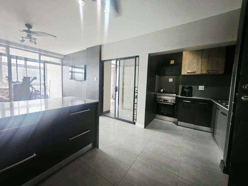 Modern open-plan kitchen and living area featuring sleek dark cabinetry, a central island, built-in appliances, and large sliding doors leading to an outdoor space.