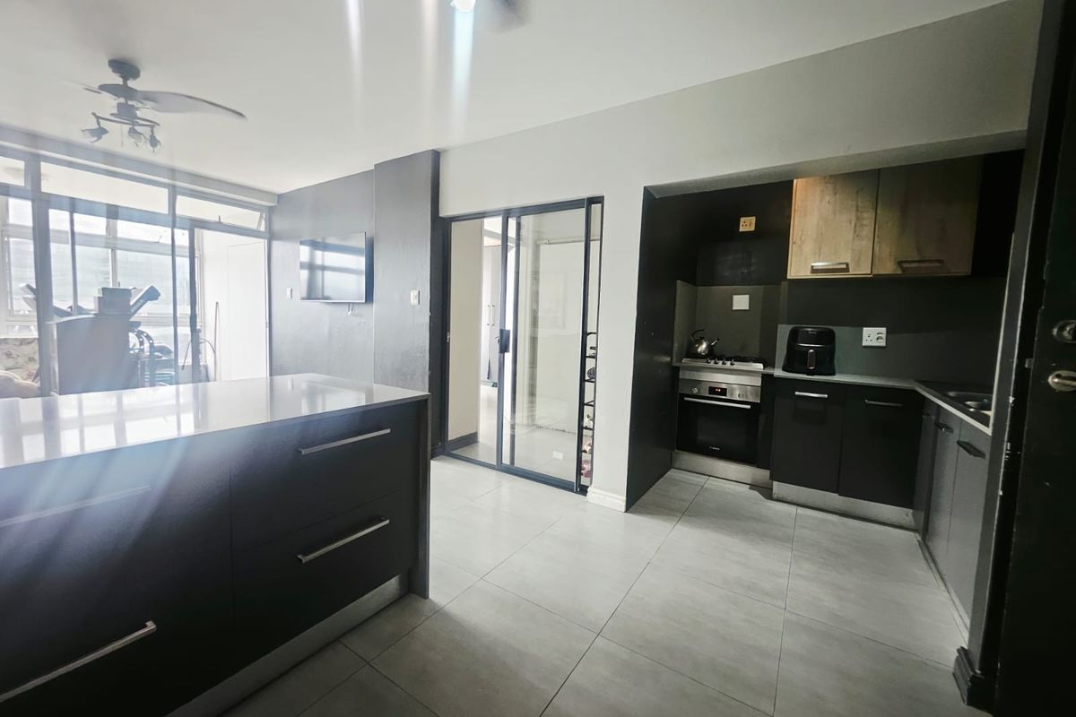 Modern open-plan kitchen and living area featuring sleek dark cabinetry, a central island, built-in appliances, and large sliding doors leading to an outdoor space.