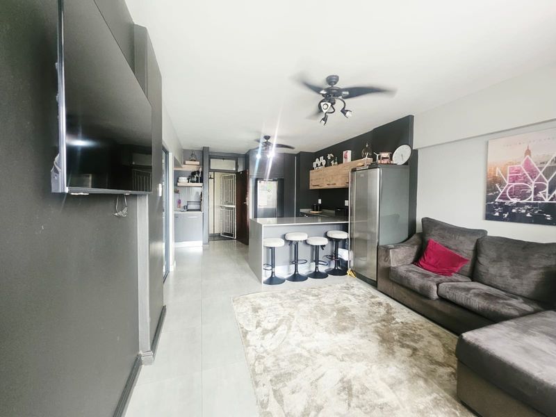 Open-plan living area featuring a modern kitchen with a central island, breakfast bar, and tiled flooring throughout.