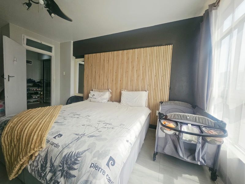 A well-maintained bedroom featuring a modern timber slat feature wall, tiled flooring, and a ceiling fan.