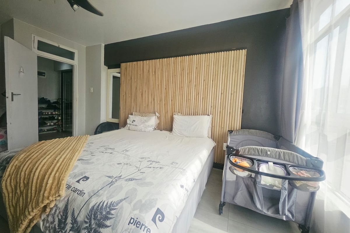 A well-maintained bedroom featuring a modern timber slat feature wall, tiled flooring, and a ceiling fan.