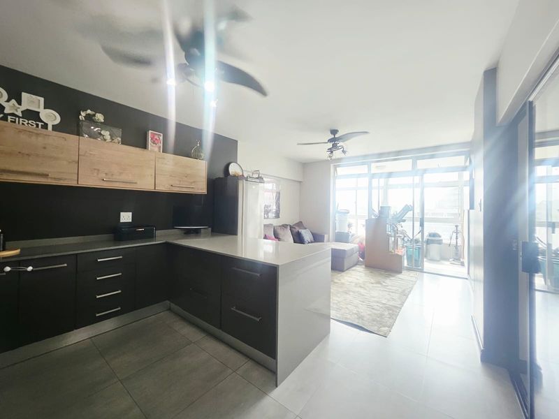 Open-plan living area featuring a modern kitchen with dark cabinetry, stone countertops, and direct access to an outdoor balcony through sliding glass doors.